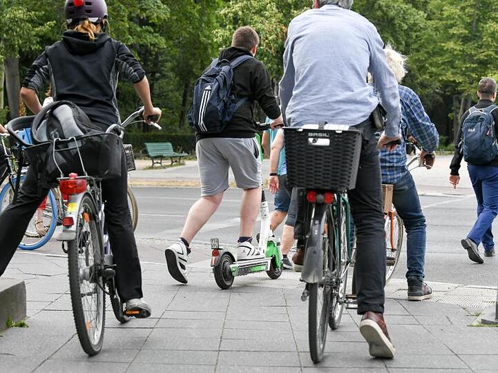 Ein E-Tretroller zwischen Fahrrädern und Autos im Straßenverkehr.