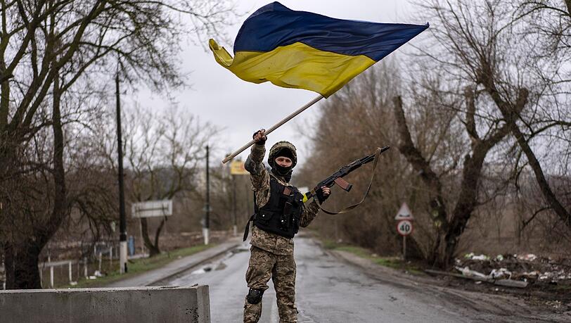 Ein ukrainischer Soldat steht an einer Straßenblockade und hält die ukrainische Flagge hoch.