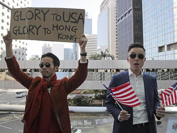 Demonstranten halten amerikanische Flaggen und ein Plakat mit der Aufschrift "Glory to USA, Glory to Hong Kong" ("Ruhm für die USA, Ruhm für Hong Kong") hoch.