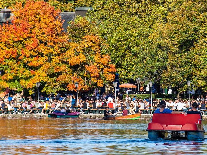 Personen in Tretbooten fahren vor dem Biergarten vom Seehaus im Englischen Garten. Foto: Lino Mirgeler/dpa/Archivbild