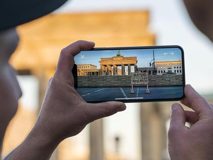 Apple-Chef Tim Cook lässt sich am Brandenburger Tor von Entwickler Peter Kolski das Projekt "MauAR" auf einem Smartphone erklären.