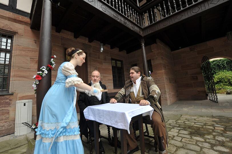 Blaustrumpf Marie Tucher (Alexandra Völkl) serviert dem Hausfreund Konrad Grübel (Christian Kaltenhäußer) Schnaps statt Bier. Vater Jobst (Mitte) hat andere Sorgen.