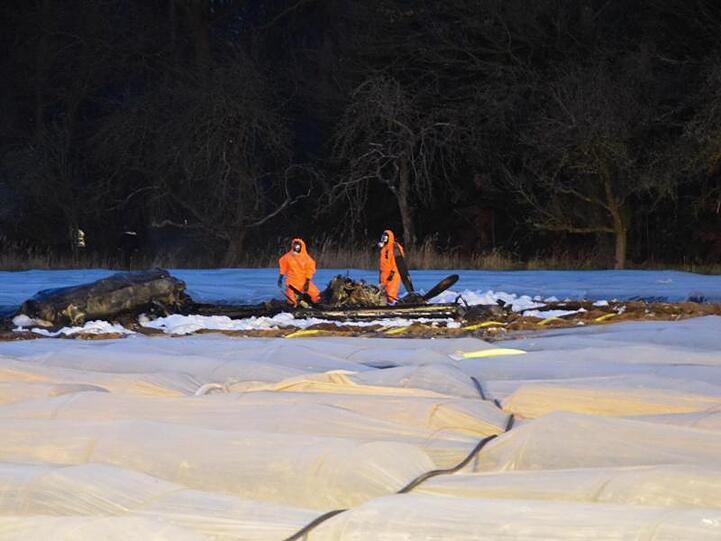 Feuerwehrleute in Schutzanzügen halten Brandwache nach dem Absturz eines Kleinflugzeugs auf einem Spargelfeld.