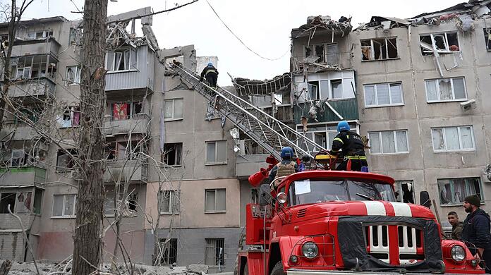 Feuerwehrleute arbeiten daran, ein Feuer zu löschen, während sie nach einem Raketenangriff nach möglichen Opfern suchen.