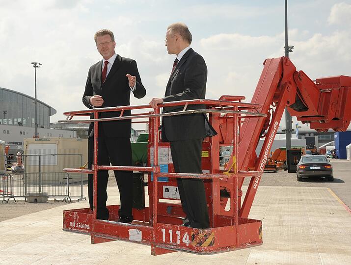 Messegeschäftsführer Eugen Eugentenmeir (rechts) und Bayerns Umweltminister Marcel Huber schauen von einer Hebebühne auf dem Messegelände in Riem auf den Aufbau der Messe IFAT.
