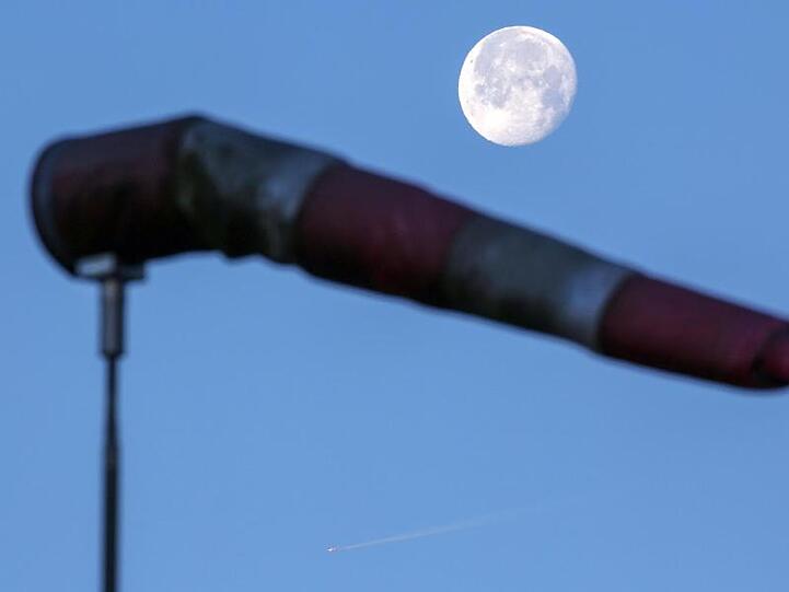 Über einem vom Wind aufgeblasenen Windsack steht kurz nach Sonnenaufgang der Mond. Foto: Thomas Warnack/dpa