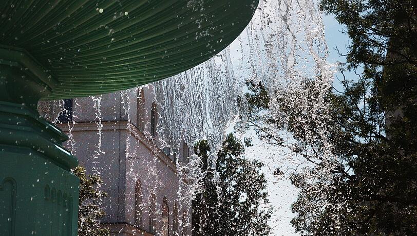 Wie fliegende Diamanten in der Sonne glänzen die Wassertropfen am Unibrunnen.
