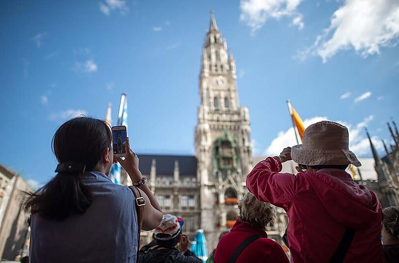 Touristen stehen am Marienplatz und fotografieren das Rathaus.