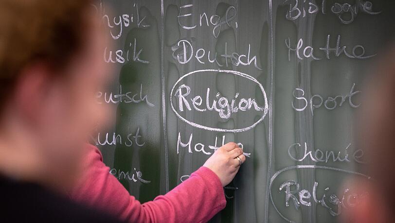 Eine Lehrerin schreibt mit Kreide einen Stundenplan mit Religionsunterricht an eine Tafel.