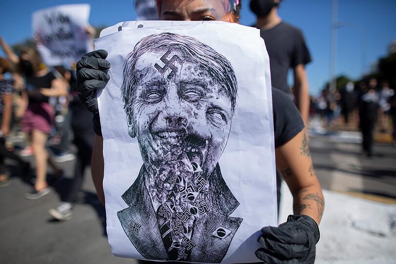 Einige Demonstranten werfen dem brasilianischen Präsidenten wegen seiner Tatenlosigkeit Genozid vor. Auf diesem Protestplakat verschwimmt Bolsonaros Gesicht mit dem Hitlers.