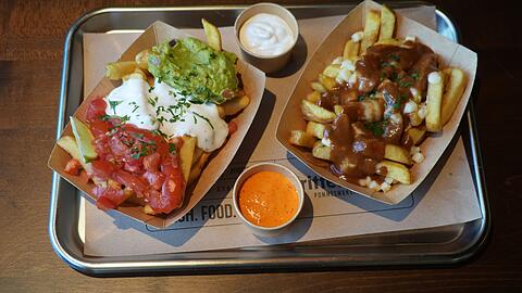 Das Prinzip bei Frittenwerk lautet: Pommes, Soße und Topping. Rechts ist das kanadische Original "Poutine" zu sehen, links die Tijuana-Variante mit Guacamole, Sour Cream und Tomaten.