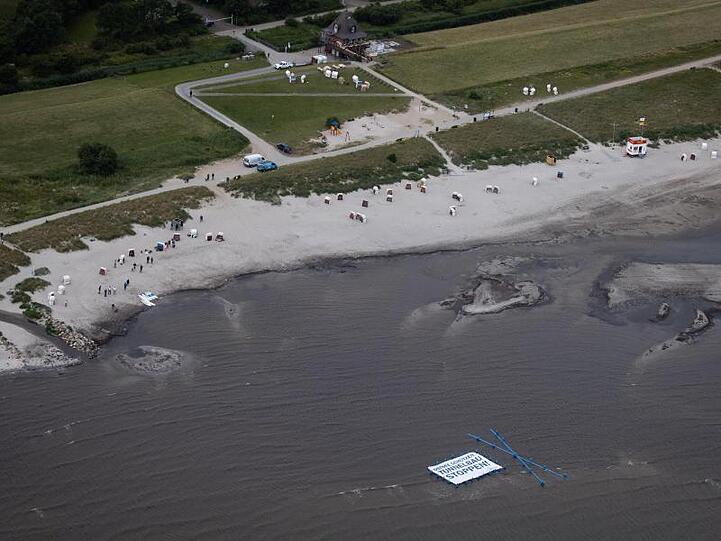 Unterstützer und Aktivisten der Protestaktion "Beltretter" halten ein Banner mit dem Text "Ostsee schützen. Tunnelbau stoppen!" und ein blaues Kreuz, während sie in der Ostsee am Naturschutzgebiet Grüner Brink nahe dem Fähranleger Puttgarden stehen.