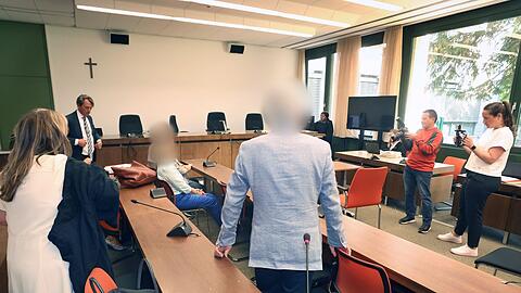 Ein Elternpaar (r und 2.v.r) sitzt und steht im Gericht neben einem Arzt (3.v.r) in der Anklagebank.