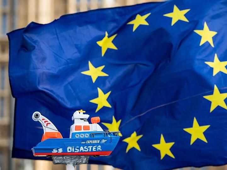 Eine EU-Flagge und ein Schiff "SS Disaster" werden bei einem Protest vor Westminster hoch gehalten. Foto: Dominic Lipinski/PA Wire/dpa