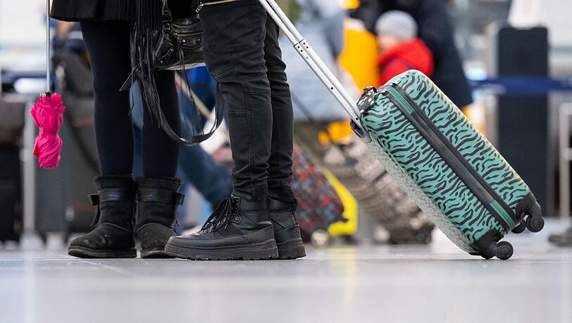 Passagiere stehen mit ihrem Gepäck an Check-in-Schaltern am Flughafen München.