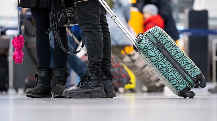 Passagiere stehen mit ihrem Gepäck an Check-in-Schaltern am Flughafen München.