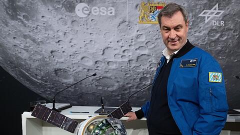 Markus Söder (CSU), Ministerpräsident von Bayern, nimmt 2024 an der Unterzeichnung einer Absichtserklärung für ein zukünftiges Mondkontrollzentrum (Moon Mission Control Centre) am Standort Oberpfaffenhofen teil und steht neben einem Modell der Raumkapsel Orion.