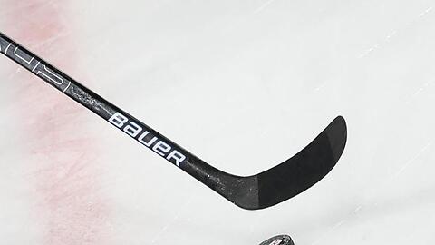 Ein Puck liegt vor einem Eishockey-Schläger auf dem Eis.