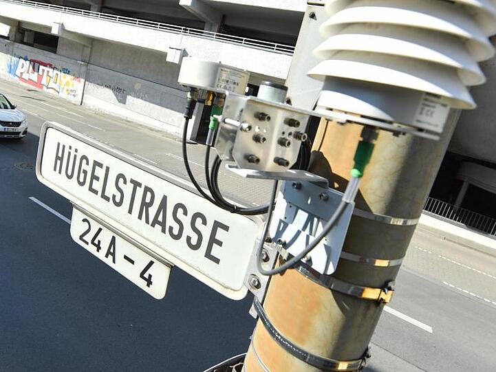 Autos fahren auf der Darmstädter Hügelstraße an einer Luftmessstation vorbei.