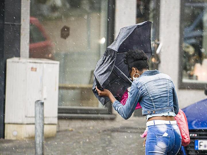 Eine Frau überquert bei starkem Wind und einsetzendem Regen eine Straße. F. Foto: Frank Rumpenhorst/dpa