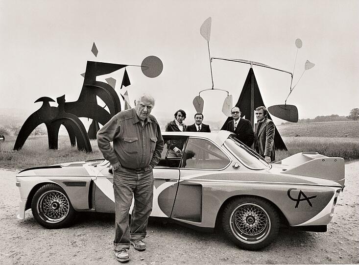 Für ein Mobile sind Autos zu schwer, aber man darf davon ausgehen, dass Alexander Calder zumindest kurz an einen solchen Einsatz dachte. Seinem Stil ist er jedenfalls treu geblieben. Die Formen, die er auf den BMW 3.0 CSL gemalt hat, könnte man ausschneiden und als Calder-Objekt aufhängen.
Der damals schon 77-jährige US-amerikanische Bildhauer war der erste, den BMW mit der künstlerischen Gestaltung eines Autos beauftragte. Und zwar für das berühmte 24-Stunden-Rennen von Le Mans. Am 14. Juni 1975 ging der ehemalige Rennfahrer und Auktionator Hervé Poulain mit dem Flitzer an den Start – und schied bereits nach sieben Stunden aus. Beim Publikum kam der bunte Rennwagen dennoch gut an, und so wurde aus der einmaligen Aktion eine Serie. Für ein Mobile sind Autos zu schwer, aber man darf davon ausgehen, dass Alexander Calder zumindest kurz an einen solchen Einsatz dachte. Seinem Stil ist er jedenfalls treu geblieben. Die Formen, die er auf den BMW 3.0 CSL gemalt hat, könnte man ausschneiden und als Calder-Objekt aufhängen.
Der damals schon 77-jährige US-amerikanische Bildhauer war der erste, den BMW mit der künstlerischen Gestaltung eines Autos beauftragte. Und zwar für das berühmte 24-Stunden-Rennen von Le Mans. Am 14. Juni 1975 ging der ehemalige Rennfahrer und Auktionator Hervé Poulain mit dem Flitzer an den Start – und schied bereits nach sieben Stunden aus. Beim Publikum kam der bunte Rennwagen dennoch gut an, und so wurde aus der einmaligen Aktion eine Serie.