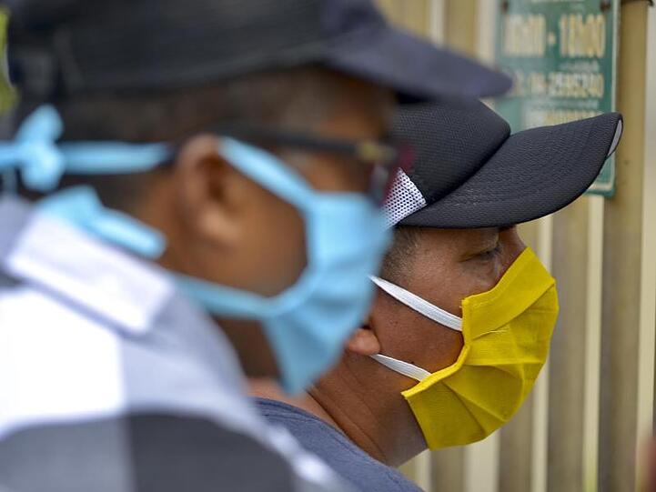 Männer mit Mundschutzmasken am Eingang des Friedhofs "Jardines de la Esperanza" in der Hafenstadt Guayaquil in Ecuador.