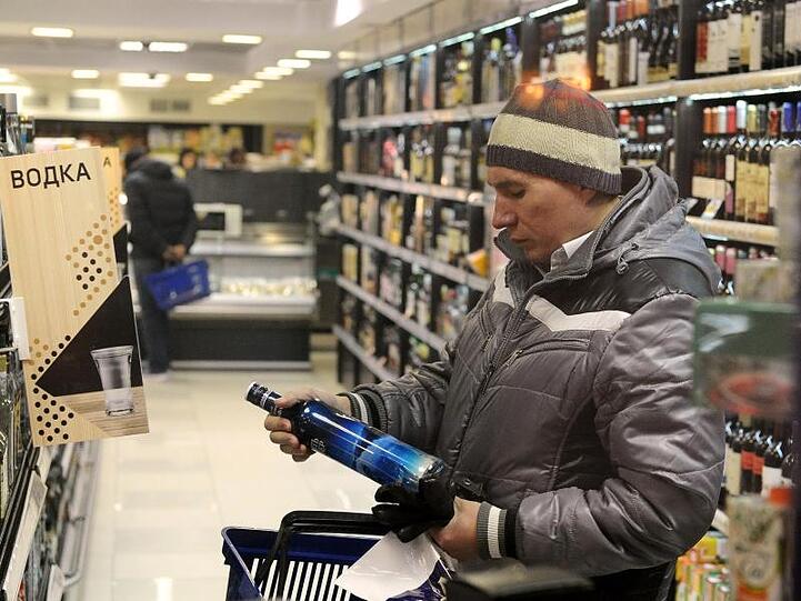 Ein Mann legt in einem Geschäft eine Flasche Wodka in seinen Einkaufskorb.