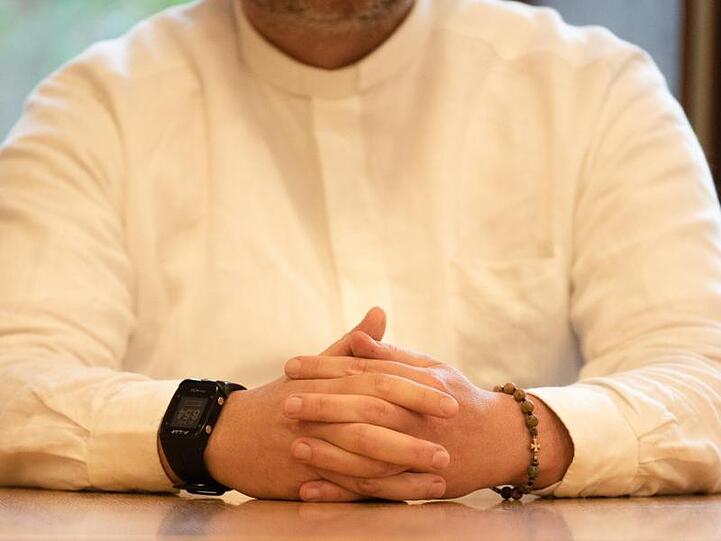 Der angeklagte Priester trägt im Gerichtssaal ein Armband mit einem Kreuz.