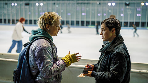 "Polizeiruf 110: Das Licht, das die Toten sehen" aus München: Bessie Eyckhoff (r., Verena Altenberger) befragt in der Eishalle Stefanie Reither (Zoë Valks) und zeigt ihr das Foto von Laura.