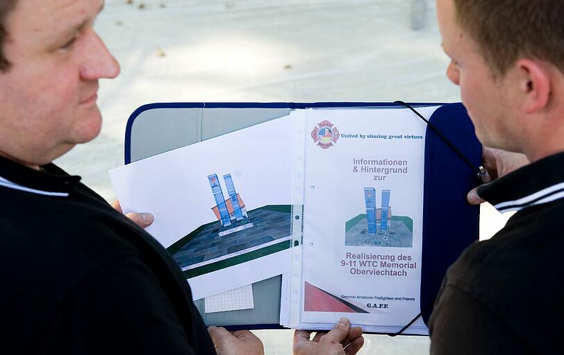 Die Vorstandsmitglieder des Vereins "German American Firefighters and Friends" (G.A.F.F.), Rainer Wild (links) und Oliver Süß, posieren vor der Baugrube mit einem Entwurf für ein Denkmal, das an die Terroranschläge auf das World Trade Center in New York erinnern soll.