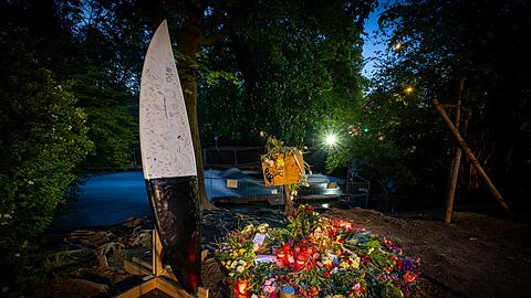 Blumen, Kerzen und Briefe liegen in den fr&uuml;hen Morgenstunden vor einem Zaun am Ufer der Eisbachwelle im Englischen Garten. Links ist ein Surfboard aufgebaut, auf dem Nachrichten und Unterschriften hinterlassen wurden. Eine Surferin, die im April auf der Eisbachwelle im Englischen Garten st&uuml;rzte, war im Krankenhaus verstorben.