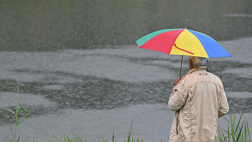 Ein Mann mir Regenschirm steht am Fluss. Müssen wir uns im Juni auf kalte, nasse Tage einstellen? +++ dpa-Bildfunk +++ Ein Mann mir Regenschirm steht am Fluss. Müssen wir uns im Juni auf kalte, nasse Tage einstellen? +++ dpa-Bildfunk +++