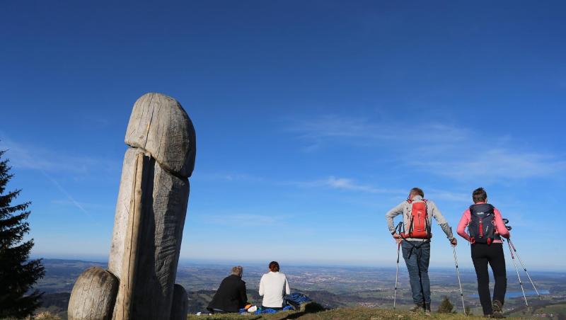 Wanderer genießen neben der zwei Meter hohen Penis-Skulptur aus Holz auf dem Grat des Grünten den Ausblick.