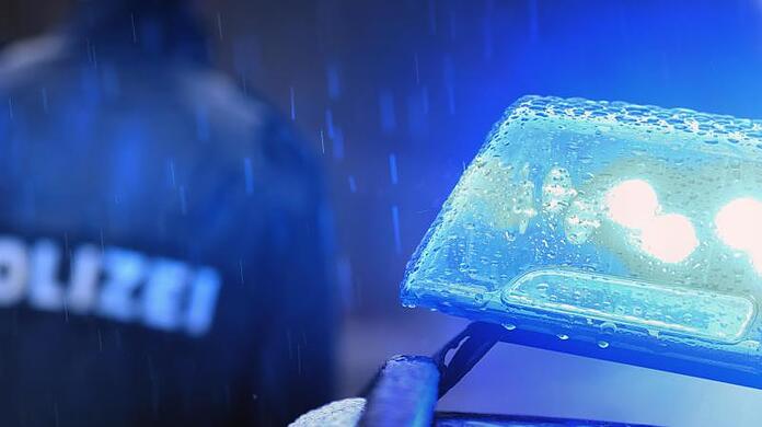 Ein Polizist steht vor einem Streifenwagen dessen Blaulicht aktiviert ist. (Symbolbild)