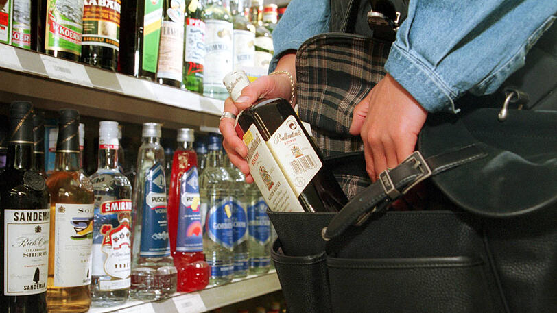 Eine Ladendiebin steckt eine Whiskey-Flasche in ihre Handtasche (Symbolbild).