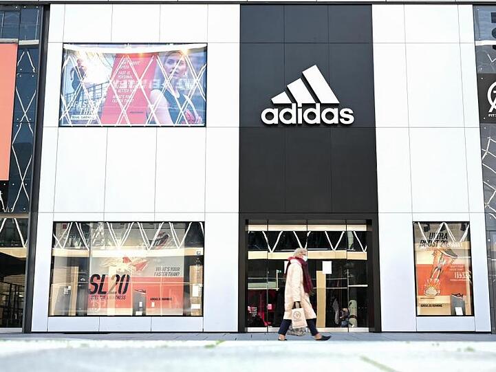 Eine Frau geht an einem Adidas-Store vorbei. Foto: Arne Dedert/dpa