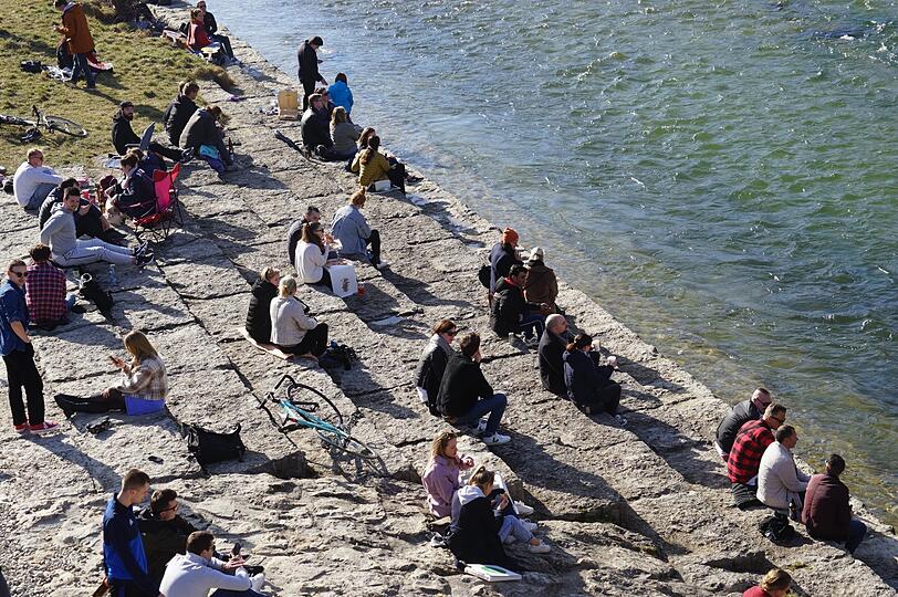 Junge Leute freuen sich über Sonne und sitzen an der Isar in München.