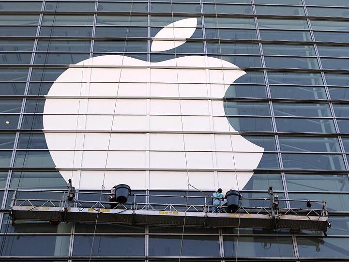Arbeiter bringen ein übergroßes Apple-Logo an einer Glasfassade an.