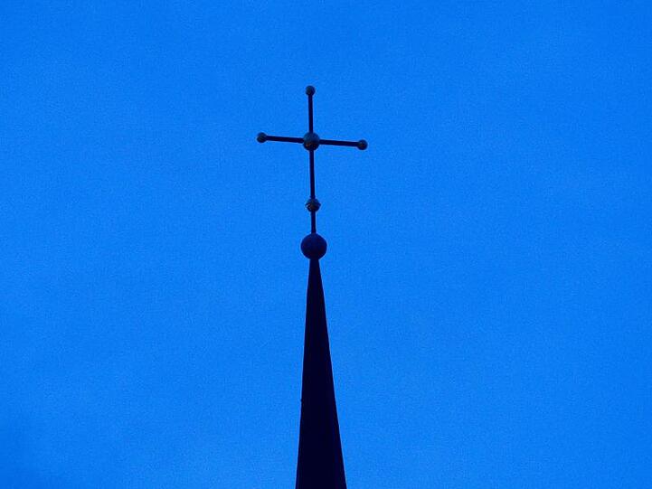 Ein Kreuz ist auf einer Kirchturmspitze zu sehen. Foto: Friso Gentsch/dpa/Symbolbild