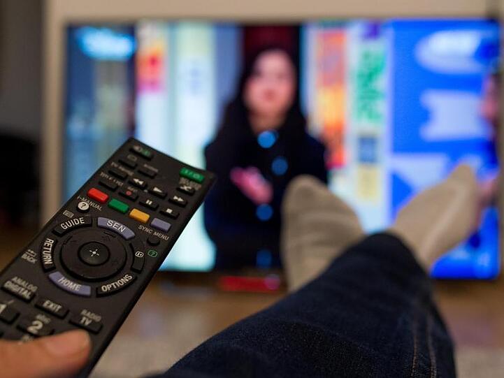 Eine Person sitzt vor einem Fernseher und hält eine Fernbedienung in der Hand. Foto: Monika Skolimowska/Archivbild