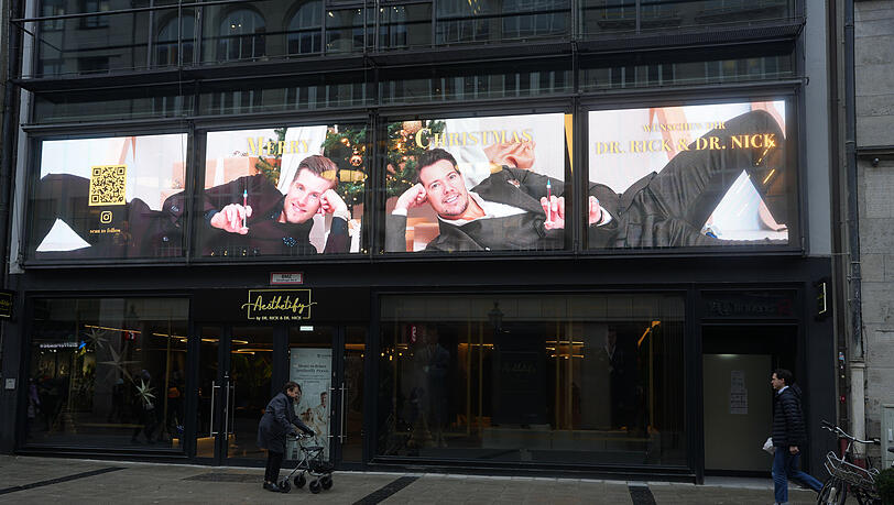 Mit breitem Zahnpastalächeln und Spritzen in der Hand wünschen die Beauty-Docs Rick und Nick frohe Weihnachten – mitten in der Sendlinger Straße. Die AZ hat Passanten gefragt, was sie davon halten.