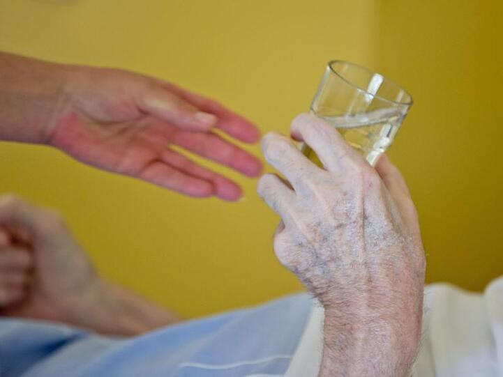 Eine Krankenpflegerin reicht einem Patienten in der Onkologie im Klinikum Nürnberg ein Glas Wasser. Foto: Daniel Karmann/Archiv