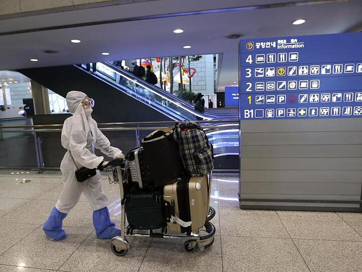 Eine Passagierin in Schutzkleidung schiebt am Flughafen Incheon einen Kofferwagen.