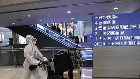 Eine Passagierin in Schutzkleidung schiebt am Flughafen Incheon einen Kofferwagen.