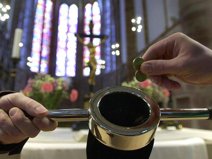 Ein Kirchenbesucher (r) steckt einige Münzen in einen Klingelbeutel.