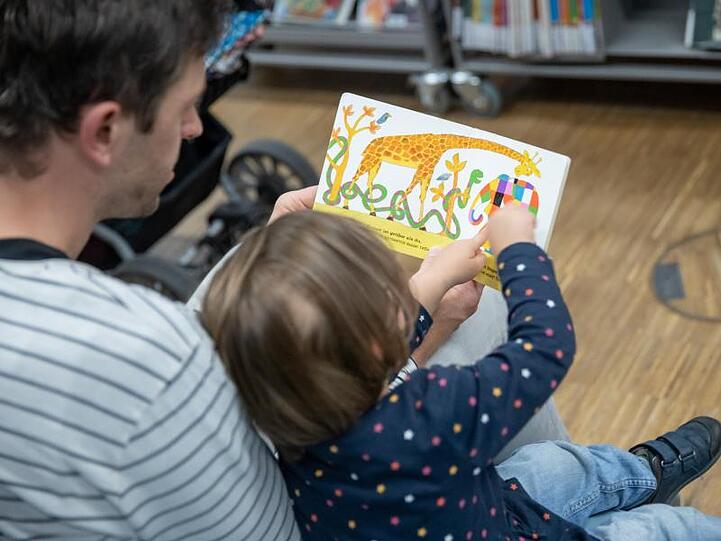 Ein Vater liest mit seiner Tochter aus einem Buch. Foto: Daniel Karmann/dpa