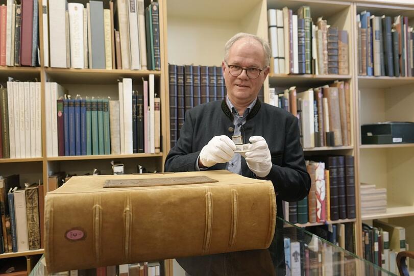 Helmut Hilz zeigt das kleinste und das schwerste Buch der Sammlung. Die wertvollen Exemplare der Bibliothek dürfen nur mit Handschuhen berührt werden.