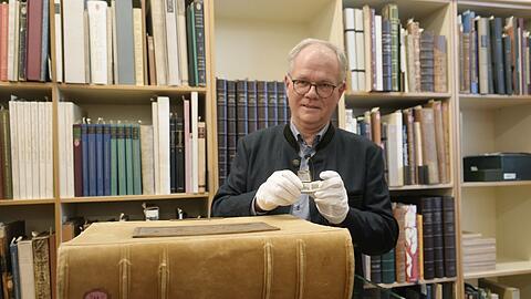 Helmut Hilz zeigt das kleinste und das schwerste Buch der Sammlung. Die wertvollen Exemplare der Bibliothek dürfen nur mit Handschuhen berührt werden.