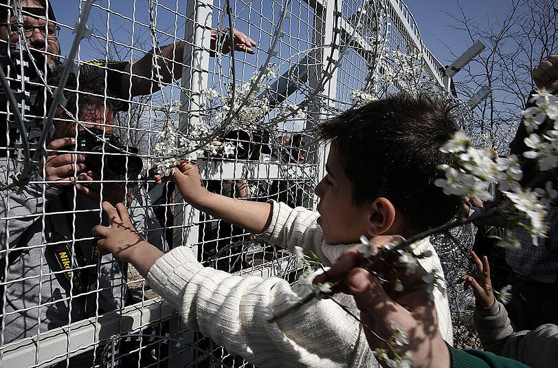 An der Grenze: Ein Flüchtlingskind steckt Blumen in den Zaun bei Idomeni zwischen Griechenland und Mazedonien.