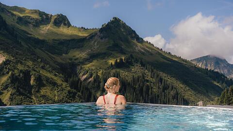 Was f&uuml;r ein Ausblick: Aus dem Infinity-Au&szlig;enpool des Genie&szlig;erhotels Alpenstern schaut man in die Dam&uuml;lser Bergwelt.
